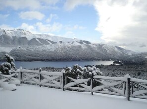 A snow-covered landscape with mountains, a lake, and a wooden fence.