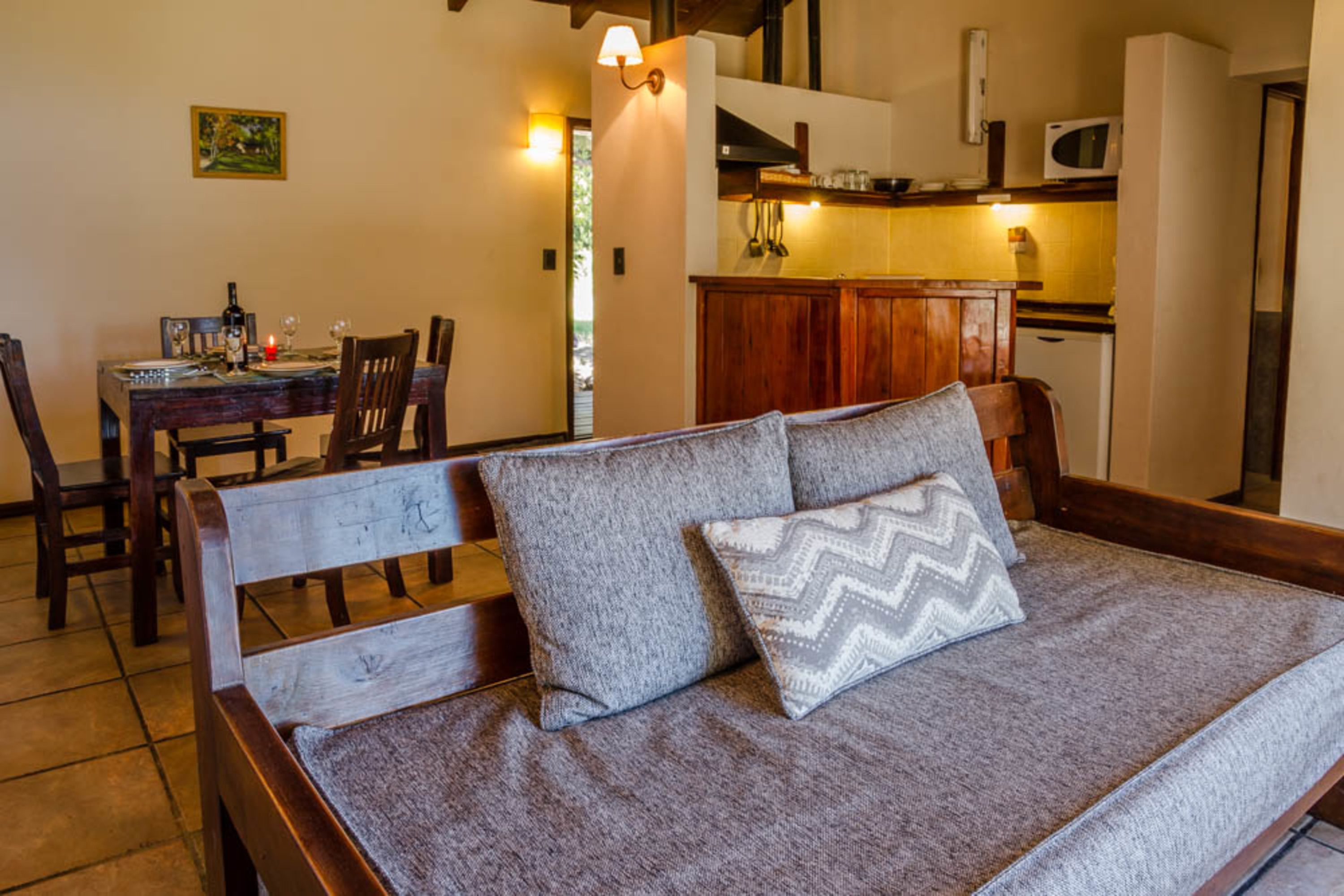 Una camera da letto con un letto in legno, due cuscini, un tavolo da pranzo con sedie e un angolo cottura con un forno a microonde.