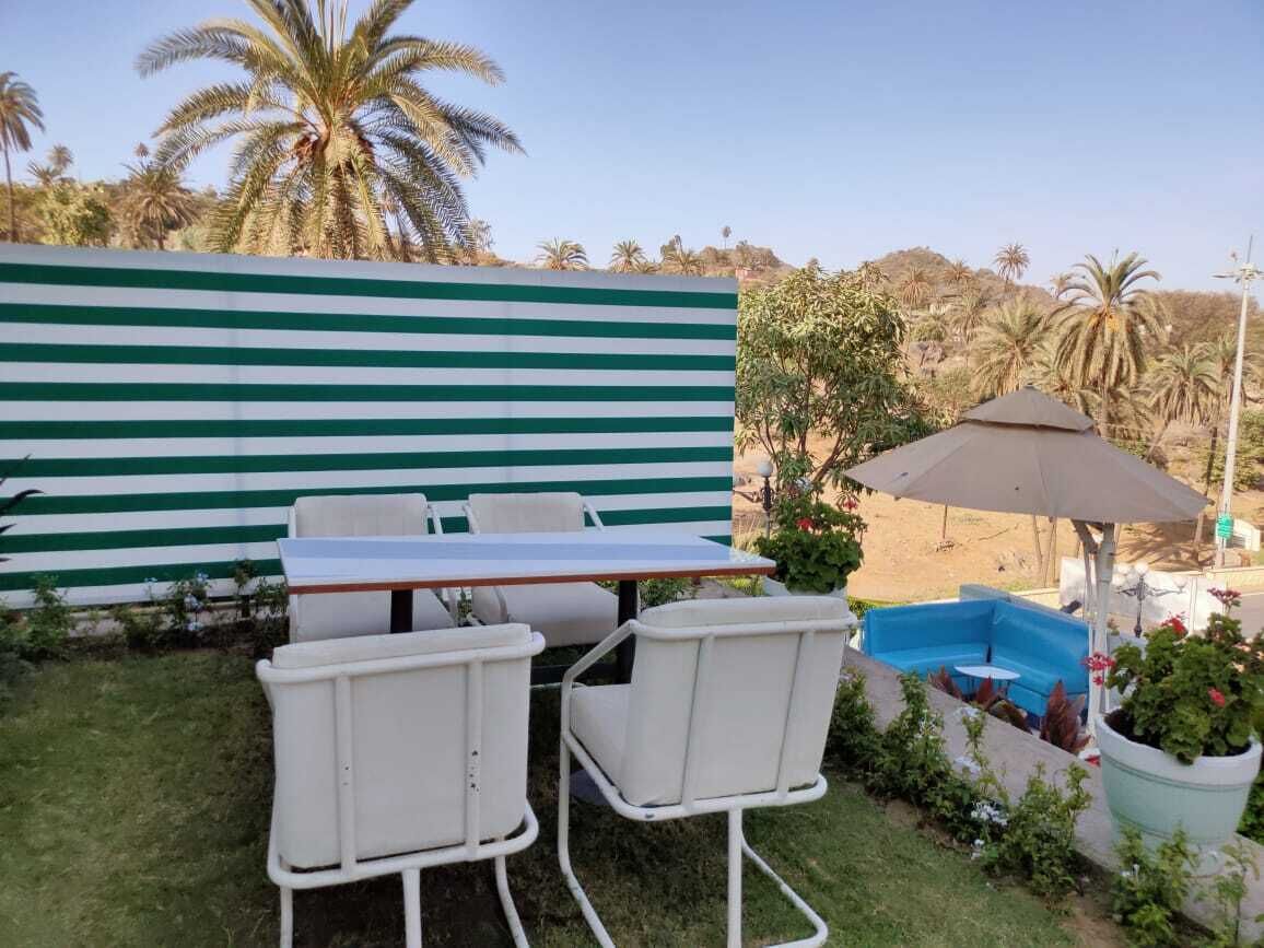 A patio with a table and chairs, a blue pool, and a striped wall.