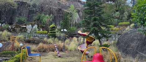 A playground with a red swing set, yellow and blue play equipment, and a slide.