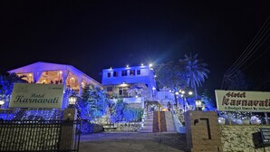 Hotel Karnavati com entrada bem iluminada, escadaria que leva ao edifício principal e placa indicando ser um hotel econômico.