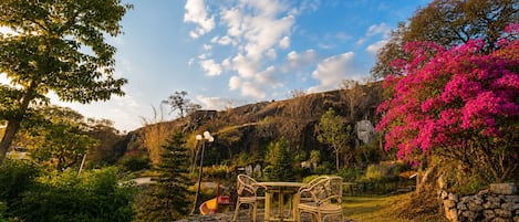 A garden with a stone table and chairs, surrounded by lush greenery and a pink flowering tree.