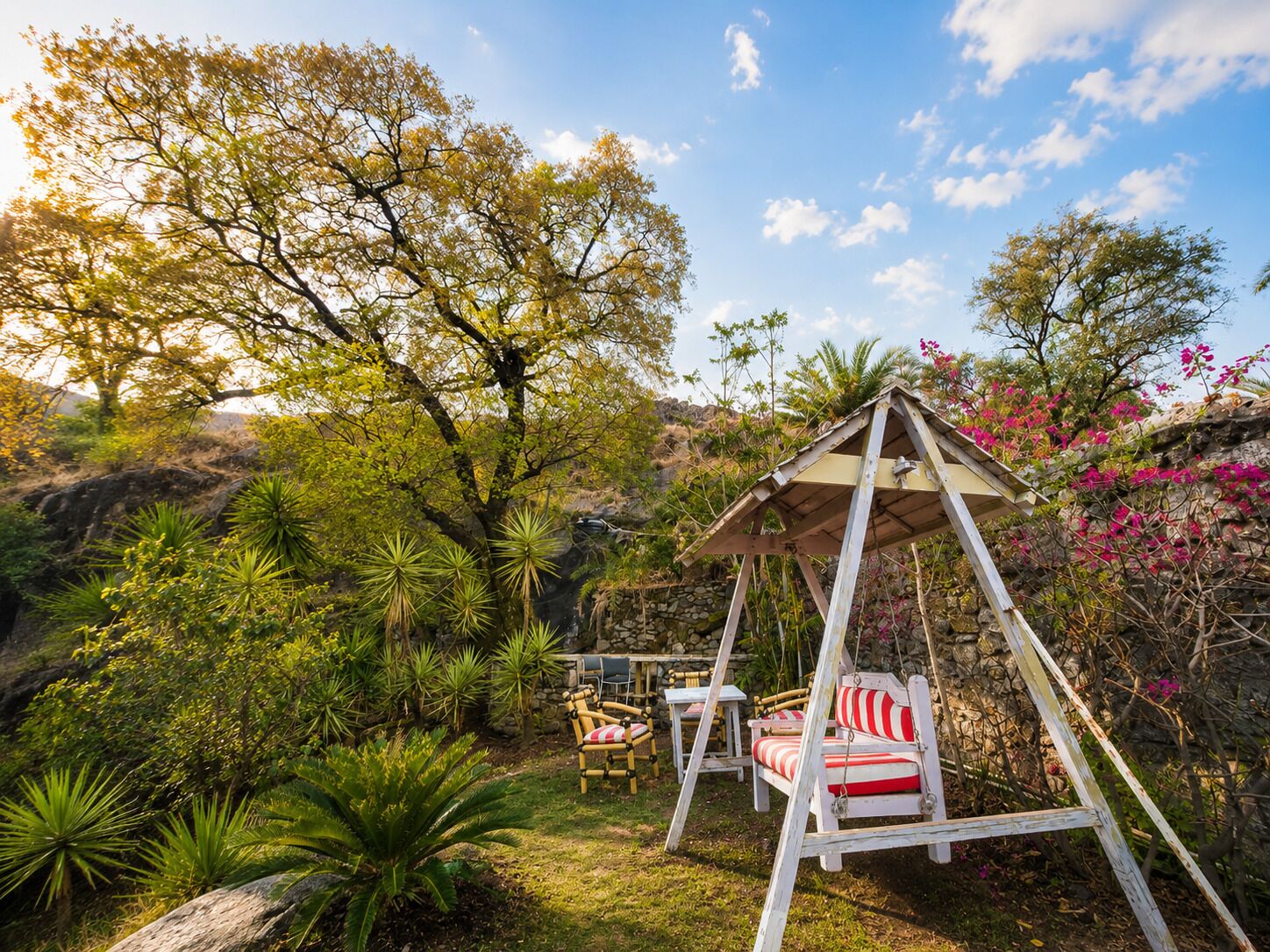 Un jardin avec une balançoire, une table et un mur en pierre.