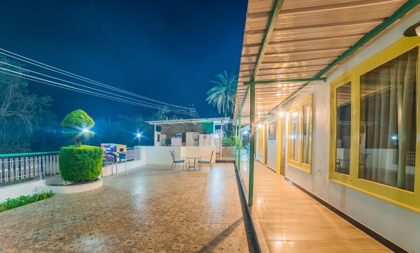 An outdoor area with a covered seating area, a small table, and chairs. There is a glass door leading to a room with a bed.
