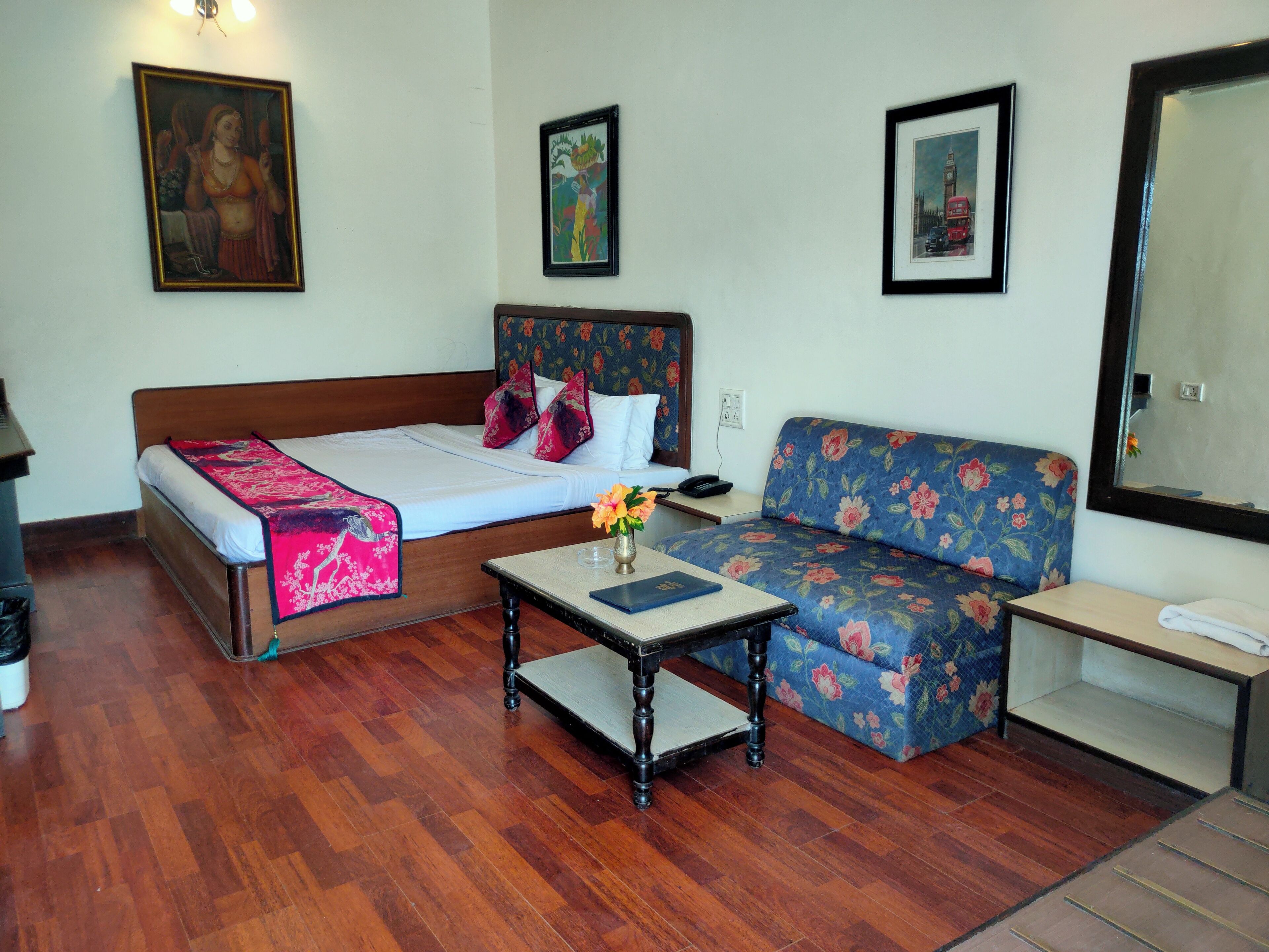 Una habitación con cama, sofá, una mesita con un florero y un espejo.