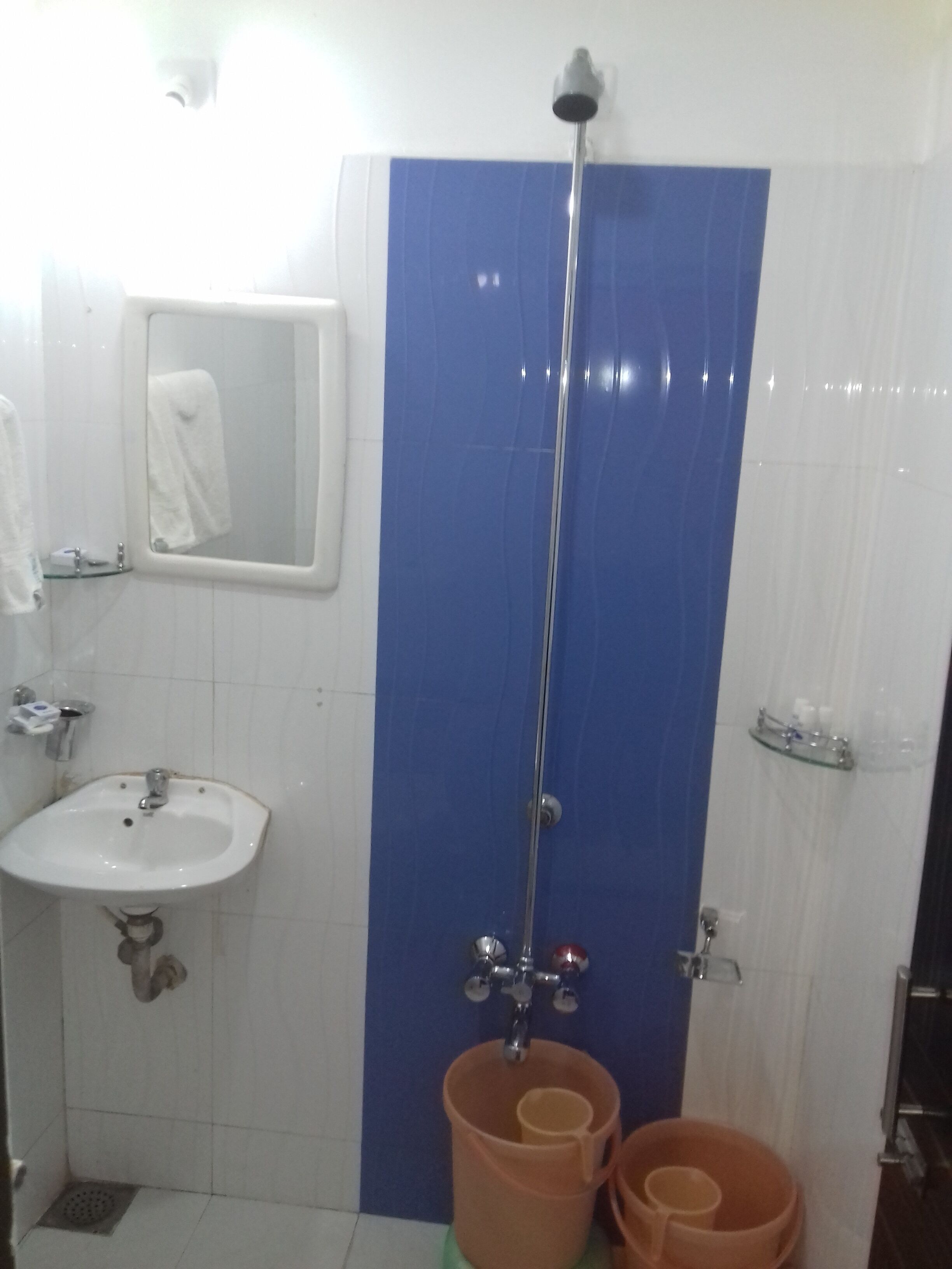 Une salle de bain équipée d’un lavabo, d’un miroir, d’une douche et de deux seaux.