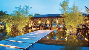 A tranquil outdoor setting with a wooden pavilion over a reflective water body, surrounded by bamboo plants and illuminated by string lights. - Flamingo Dai Lai Resort - Managed by Flamingo Hotels & Resorts (Xuan Hoa)