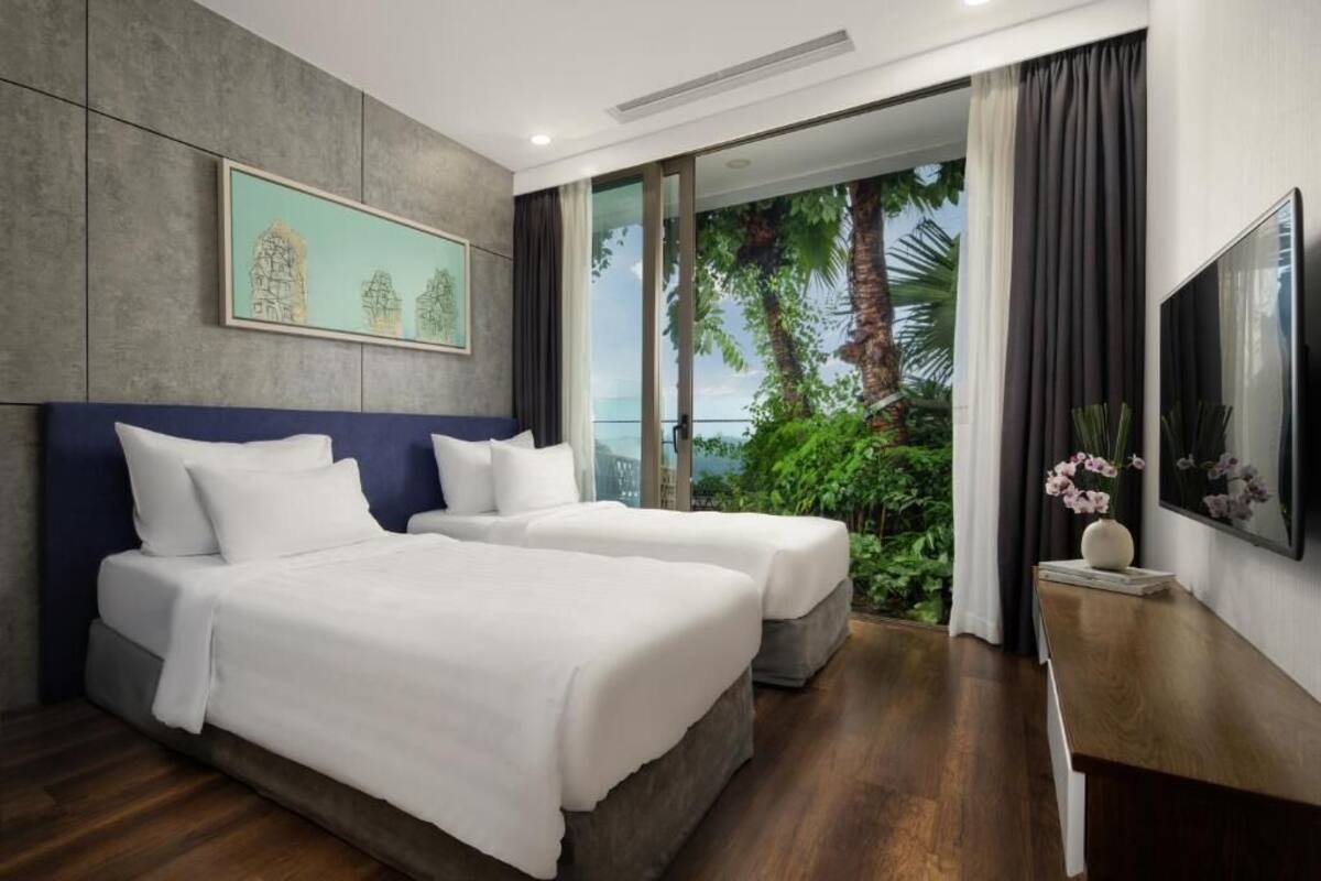 Ett modernt hotellrum med två sängar, ett stort fönster med utsikt över grönområden och en platt-TV som är monterad på väggen.