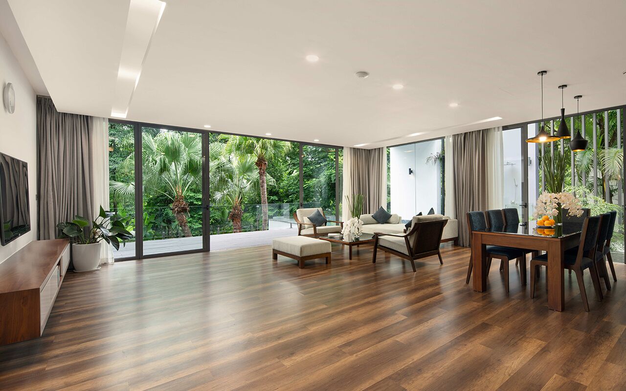 A spacious living room with a wooden floor, large windows, and a dining area with a table and chairs.