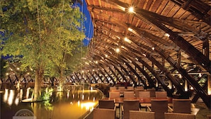 An indoor dining area with a thatched roof, wooden beams, and tables and chairs arranged for guests. - Flamingo Dai Lai Resort - Managed by Flamingo Hotels & Resorts (Xuan Hoa)