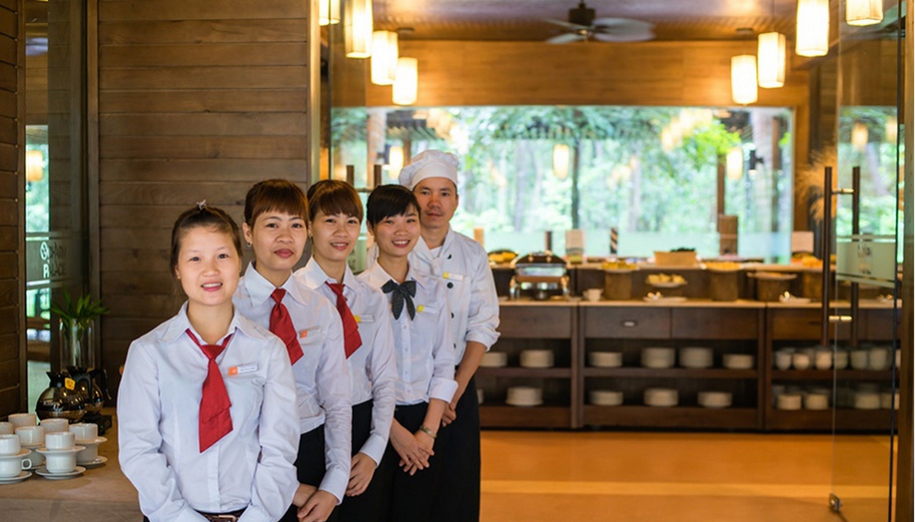 A group of people in a restaurant with a wooden interior and a view of greenery outside.