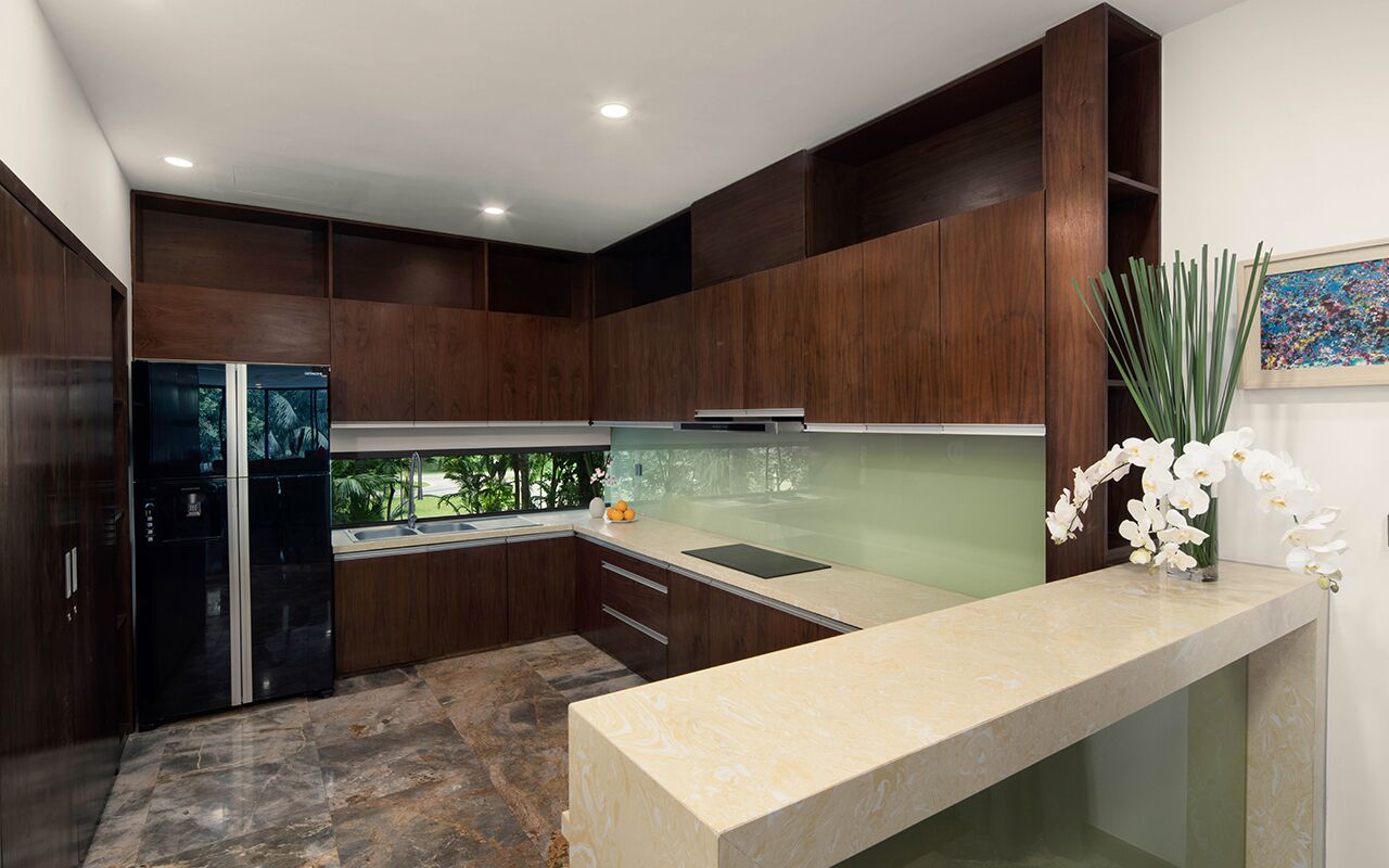 Eine moderne Küche mit dunklen Holzschränken, einem schwarzen Kühlschrank, einer Marmorarbeitsplatte und Blick auf Grünflächen.