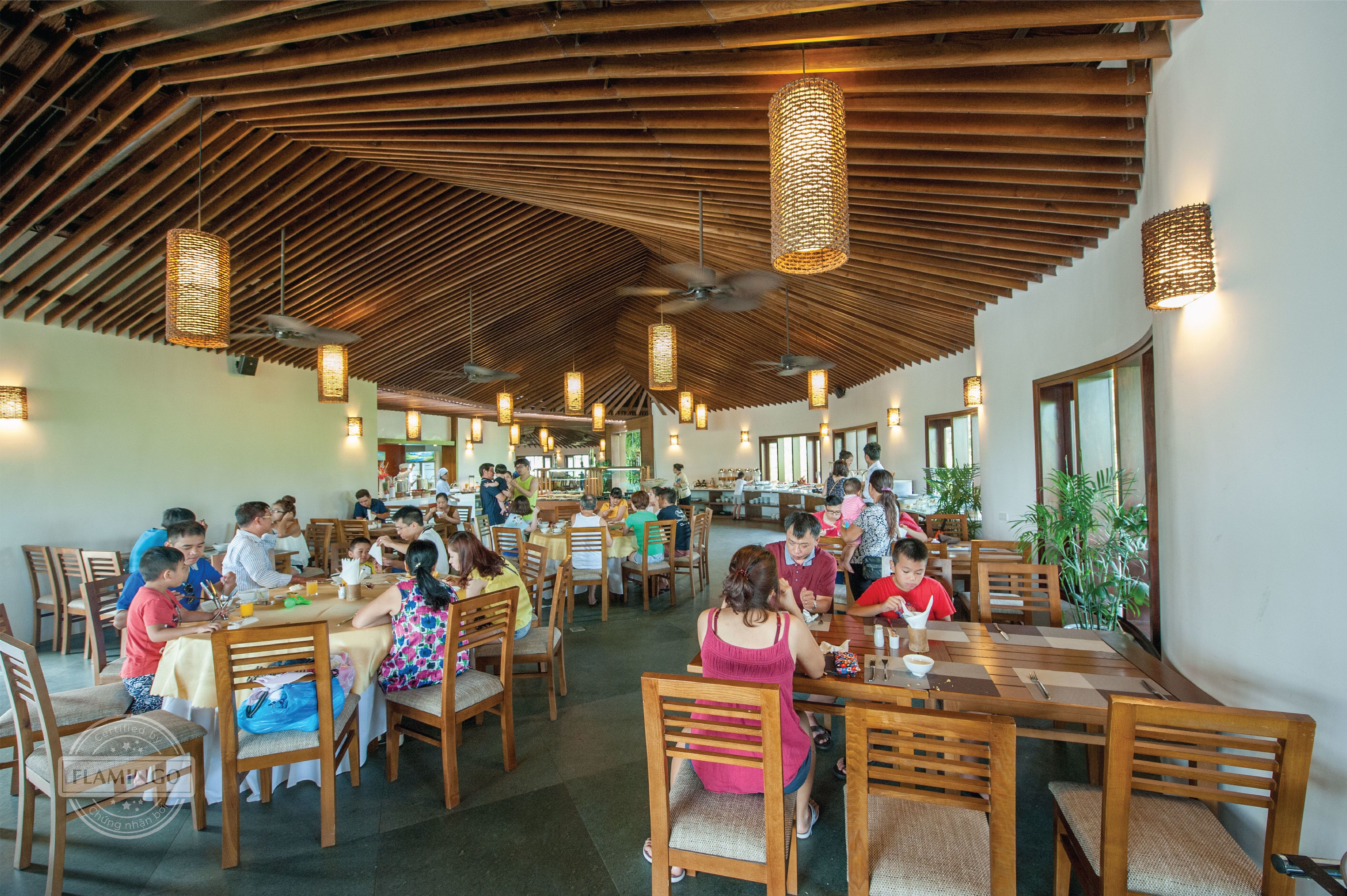 Un vaste espace dédié à la salle à manger, avec des tables et des chaises en bois, des ventilateurs de plafond et des luminaires suspendus.
