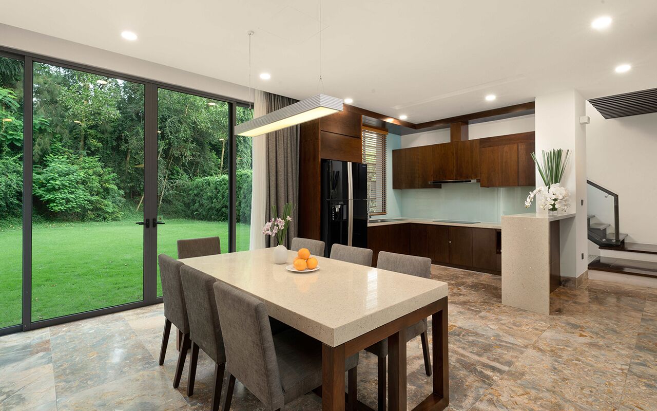 Une cuisine moderne avec un coin repas, de grandes fenêtres et une vue sur un jardin luxuriant.