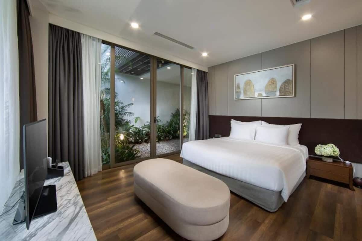 Ett modernt hotellrum med en stor säng, en platt-TV, en soffa och utsikt över grönområden genom glasdörren.