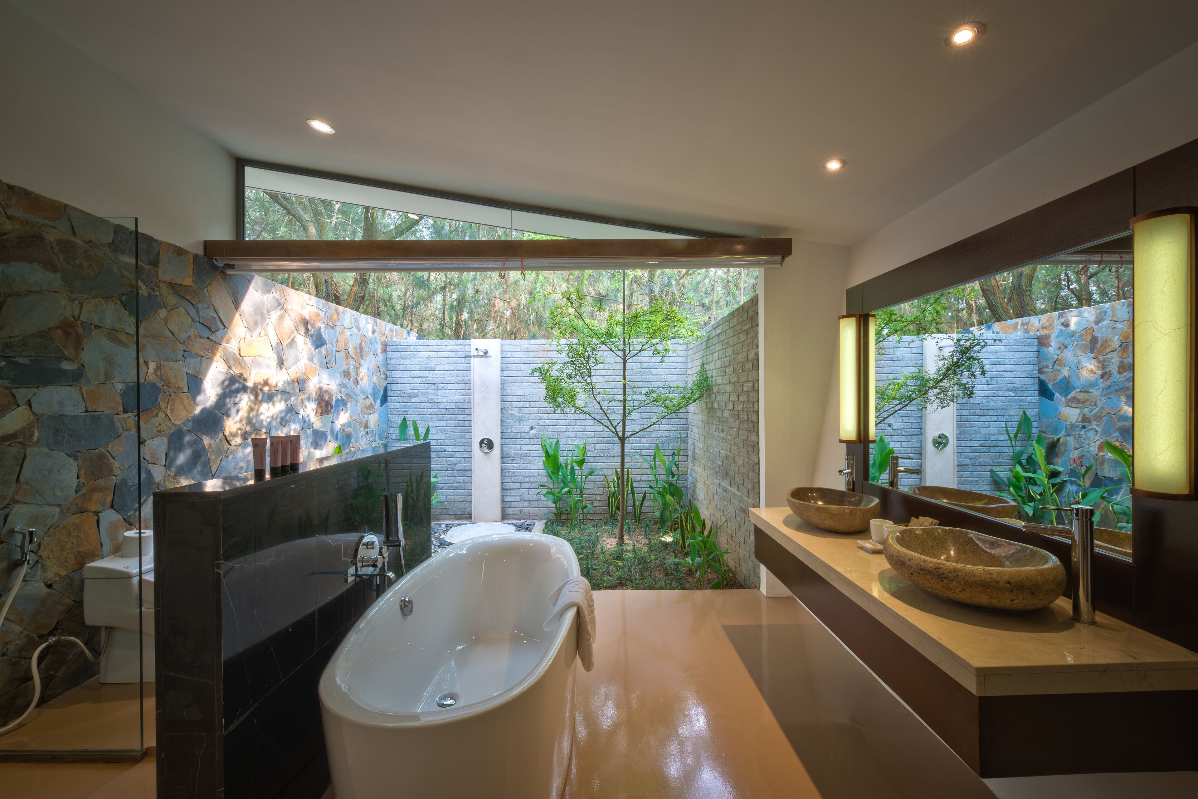 A modern bathroom with a freestanding bathtub, a large mirror, and a stone wall.