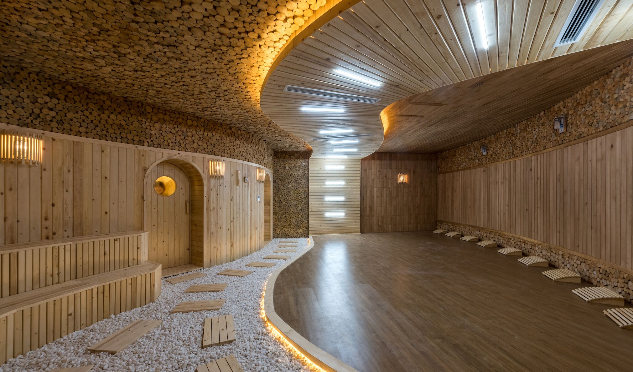 A sauna with wooden walls and benches, a curved ceiling, and a pebbled floor.