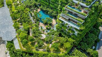 An aerial view of a hotel with a central swimming pool surrounded by lush greenery, multiple balconies, and a modern architectural design.