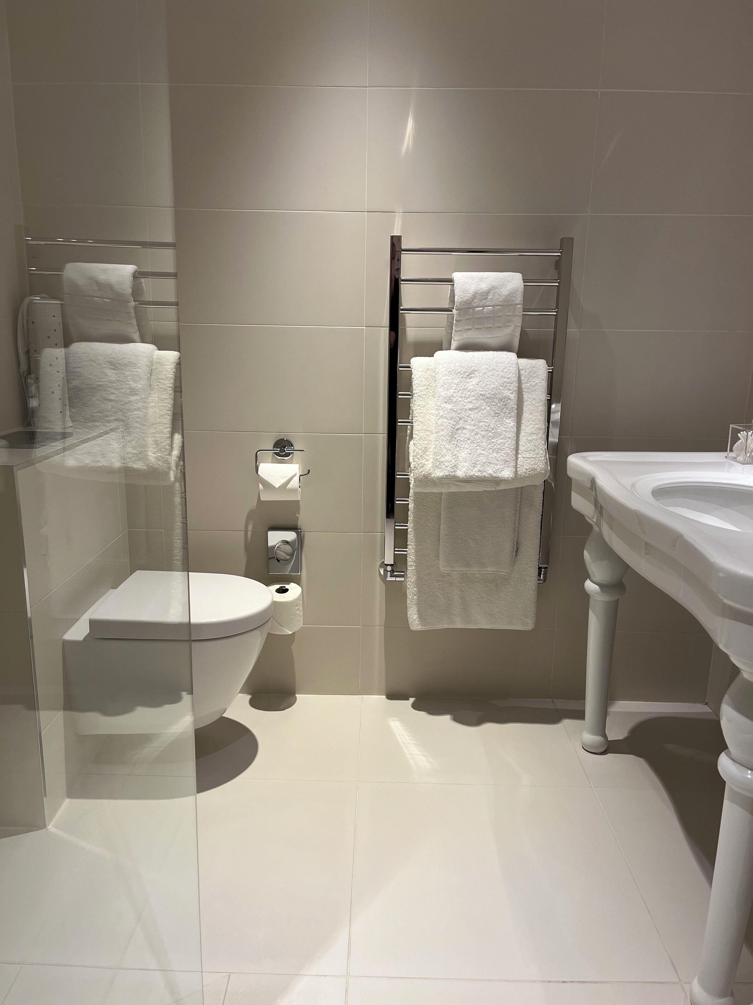 A modern bathroom with a glass partition, a toilet, a towel rack, and a sink.
