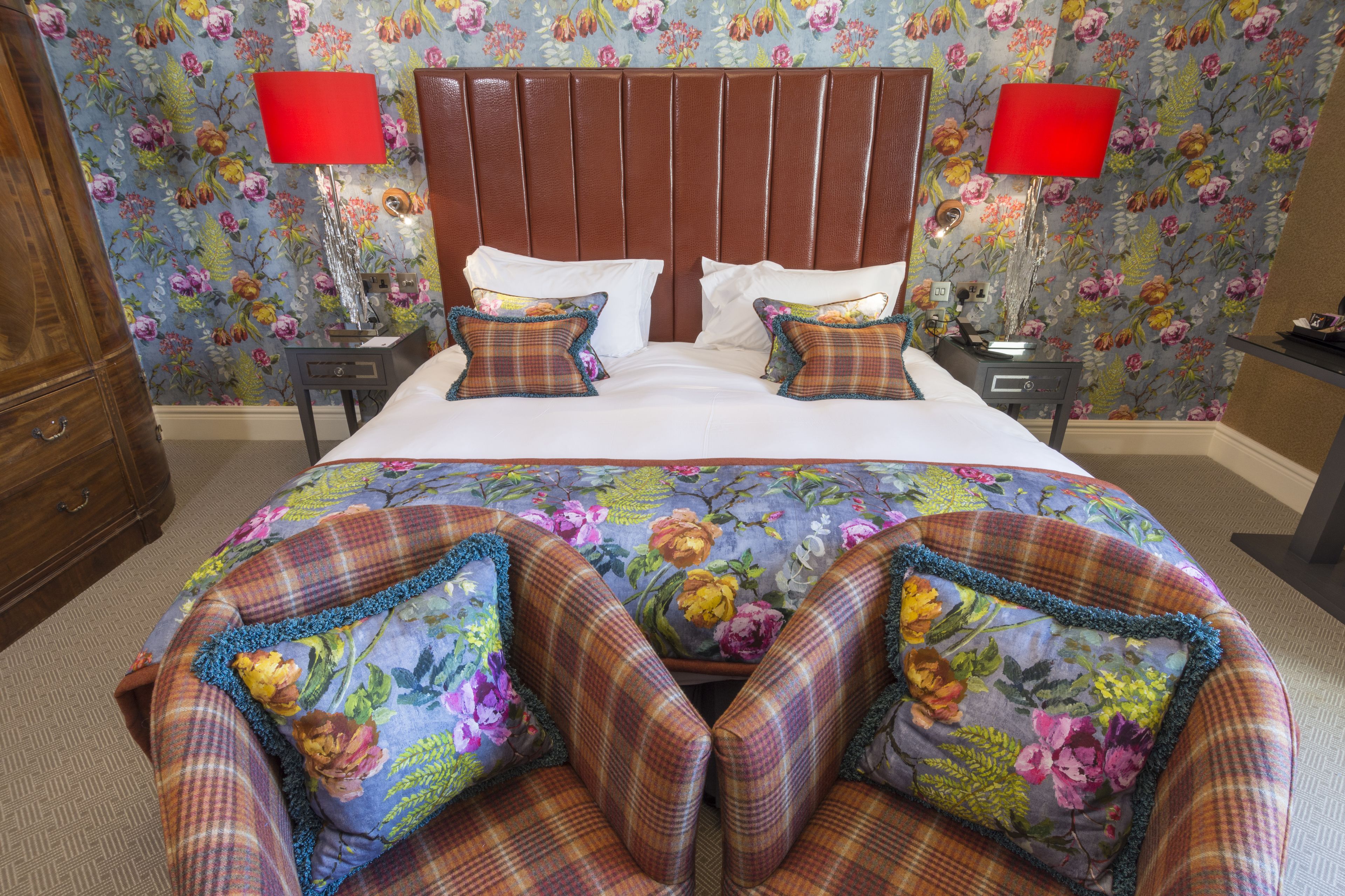Habitación de hotel con una cama grande, dos mesitas de noche y un cabecero estampado con motivos florales.