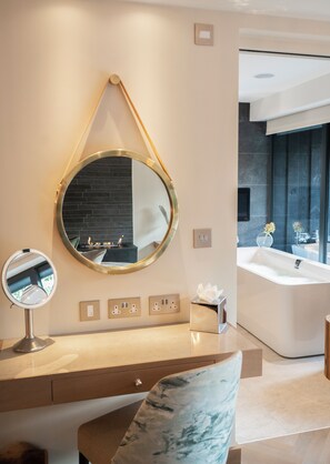 Une salle de bain moderne avec un grand miroir rond, un meuble-lavabo doté d’un plan en marbre, une baignoire et une grande fenêtre qui laisse entrer la lumière naturelle.