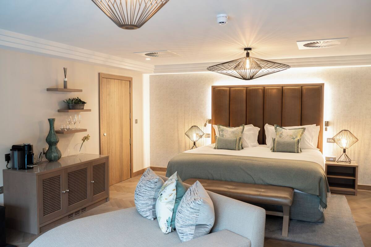 A modern bedroom with a large bed, bedside lamps, a bench, and a cabinet with decorative items.