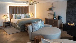 A modern bedroom with a large bed, a sofa, a small table, and a fireplace. - Storrs Hall Hotel (Windermere)
