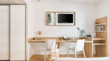 A modern hotel room with a bed, a desk with a computer, a TV, and a small kitchenette.