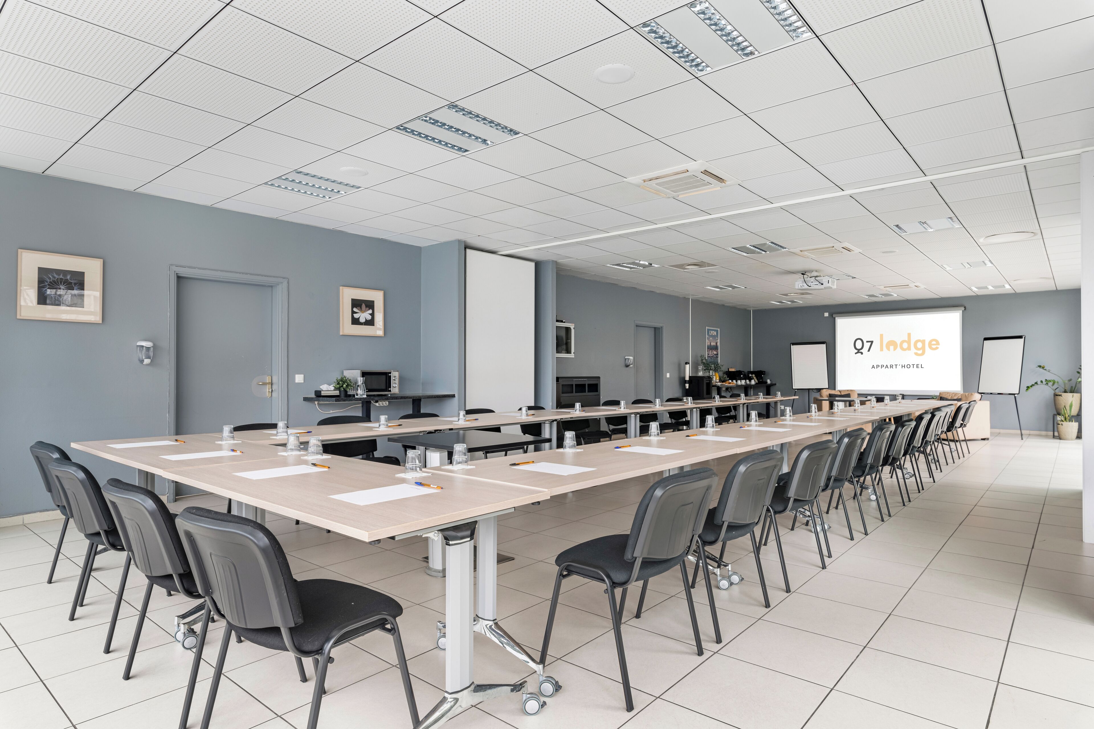 A conference room with a long table, chairs, a projector screen, and a presentation screen.