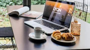 Een laptop op een tafel met een kop koffie, een bord croissants en een decoratieve vaas.