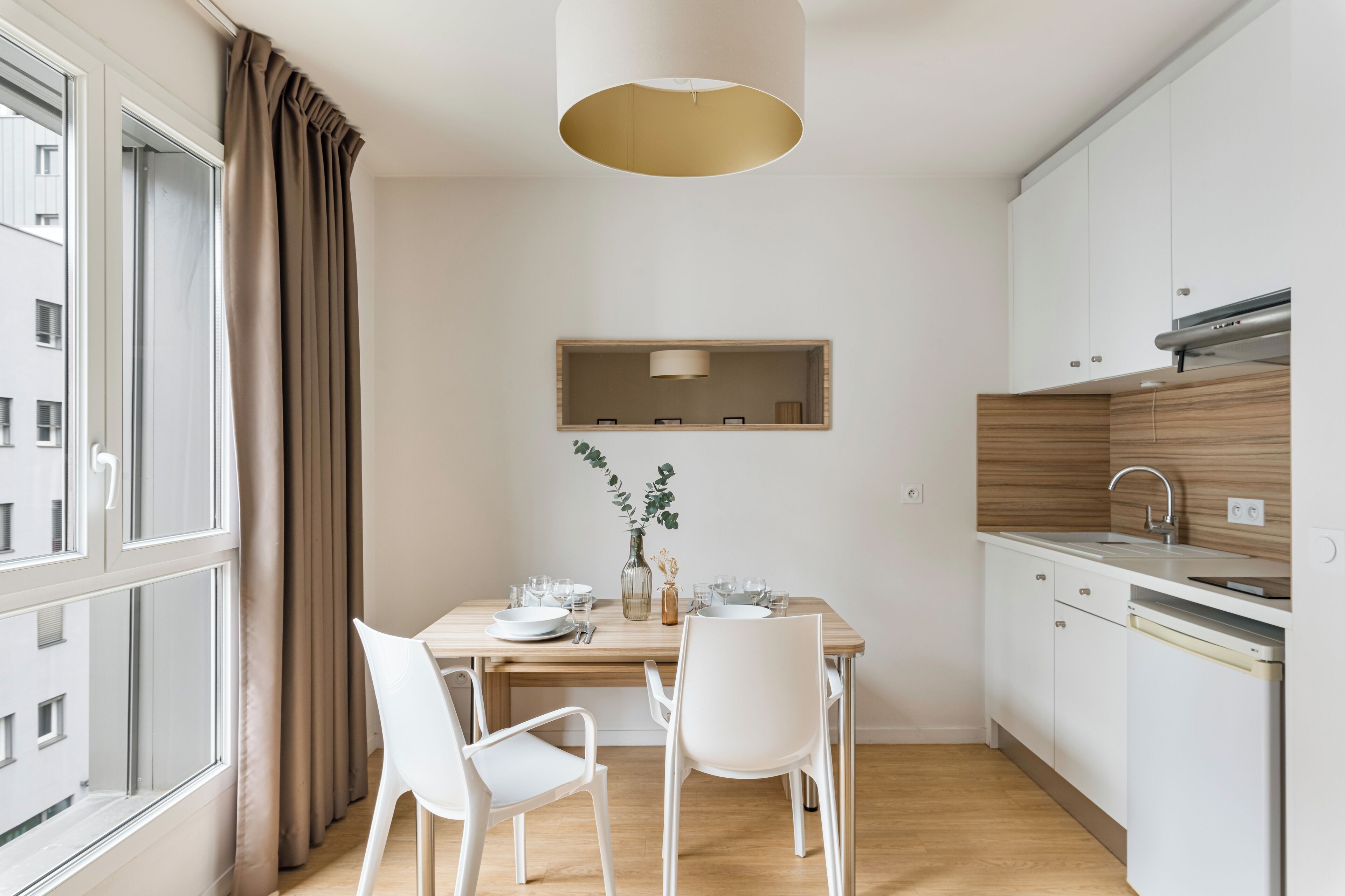 Une cuisine moderne avec des meubles blancs, un plan de travail en bois et un coin repas avec une table dressée pour deux personnes.