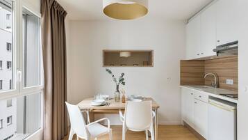 Une cuisine moderne avec des meubles blancs, un plan de travail en bois et un coin repas avec une table dressée pour deux personnes.