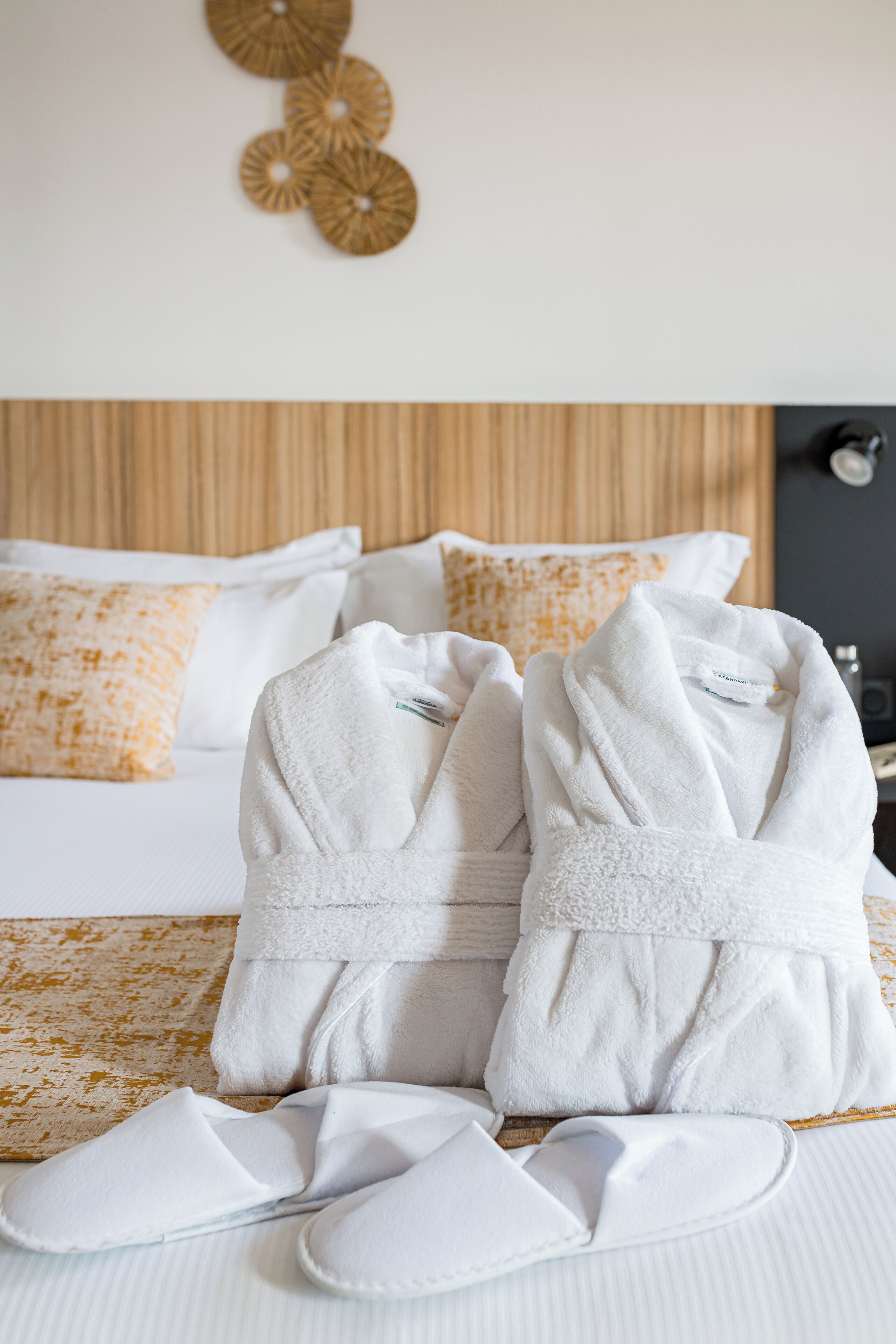 A neatly made bed with white bedding, a wooden headboard, and a decorative wall piece above.