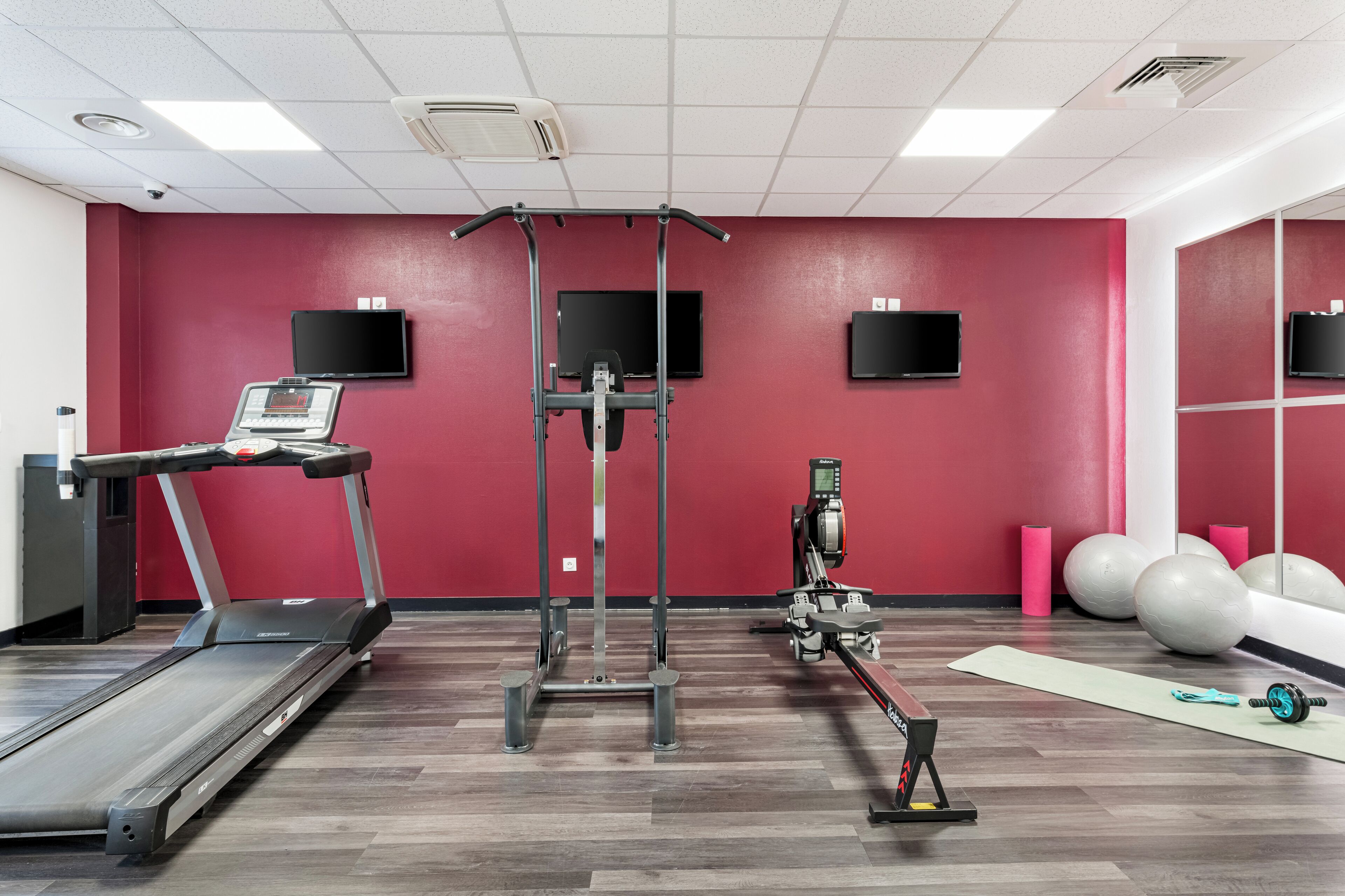 Un gimnasio con cinta de correr, máquinas de pesas y pelotas de ejercicio.