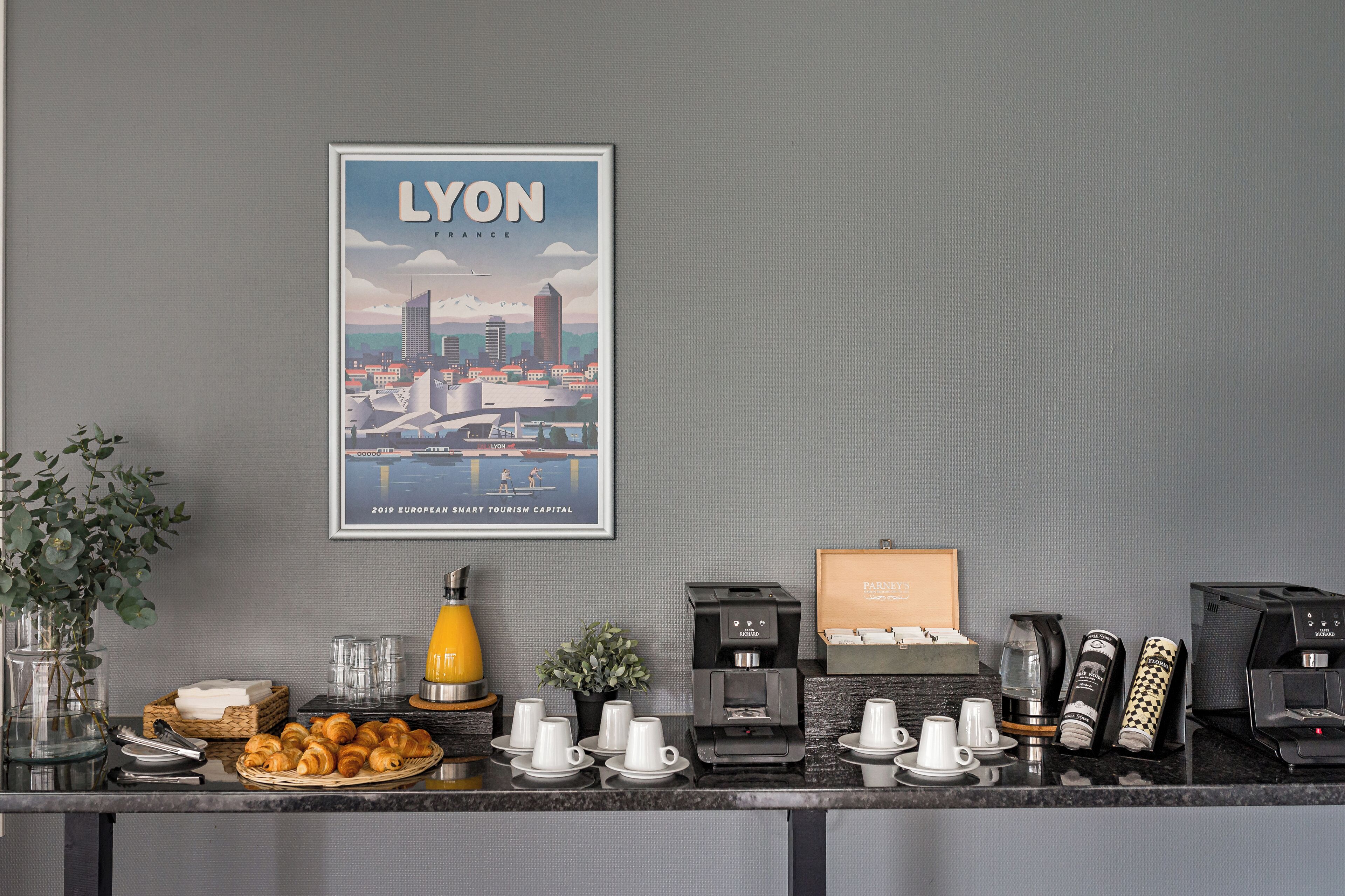 Ein Frühstücksbuffet mit Croissants, Kaffeeautomaten und einem Stadtbildplakat von Lyon.
