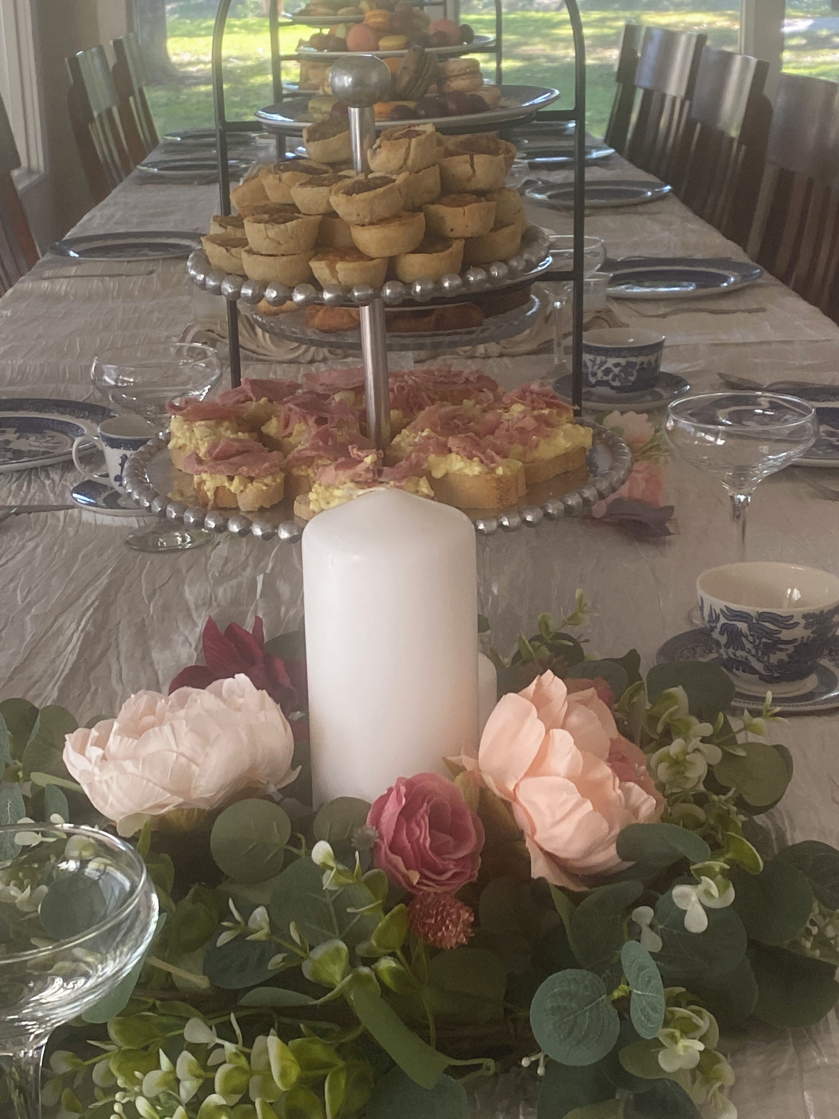 Mesa posta para refeição com suporte para sobremesas de três andares, centros de mesa florais e uma vela grande.