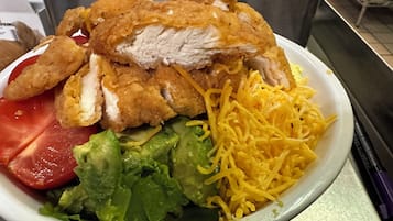 Un plato de comida con pollo, lechuga, queso rallado y rodajas de tomate.