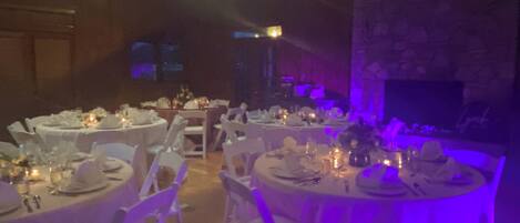 Un salón de banquetes con mesas redondas dispuestas para comer, sillas blancas y manteles blancos.