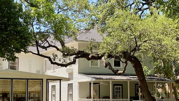 A two-story house with a covered porch, stone foundation, and large windows. - Inn On The River (Glen Rose)