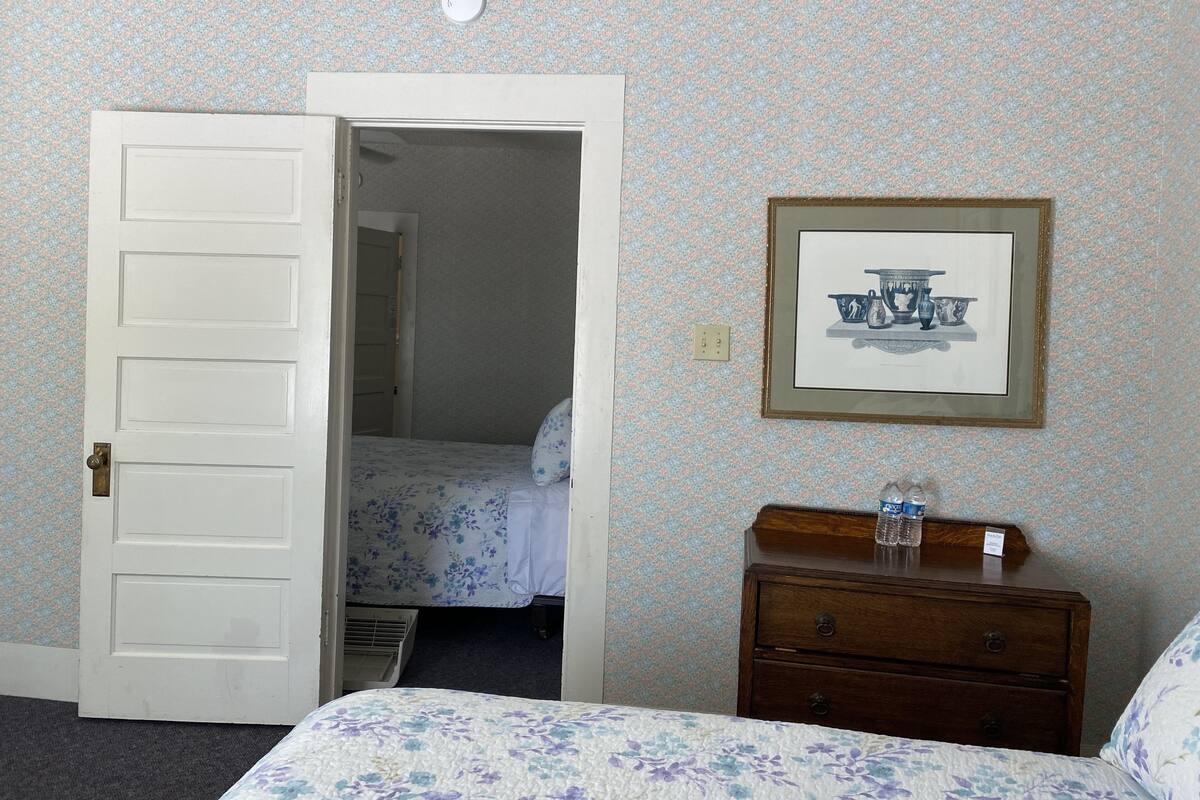 A bedroom with a bed, a dresser, and a door leading to another room.