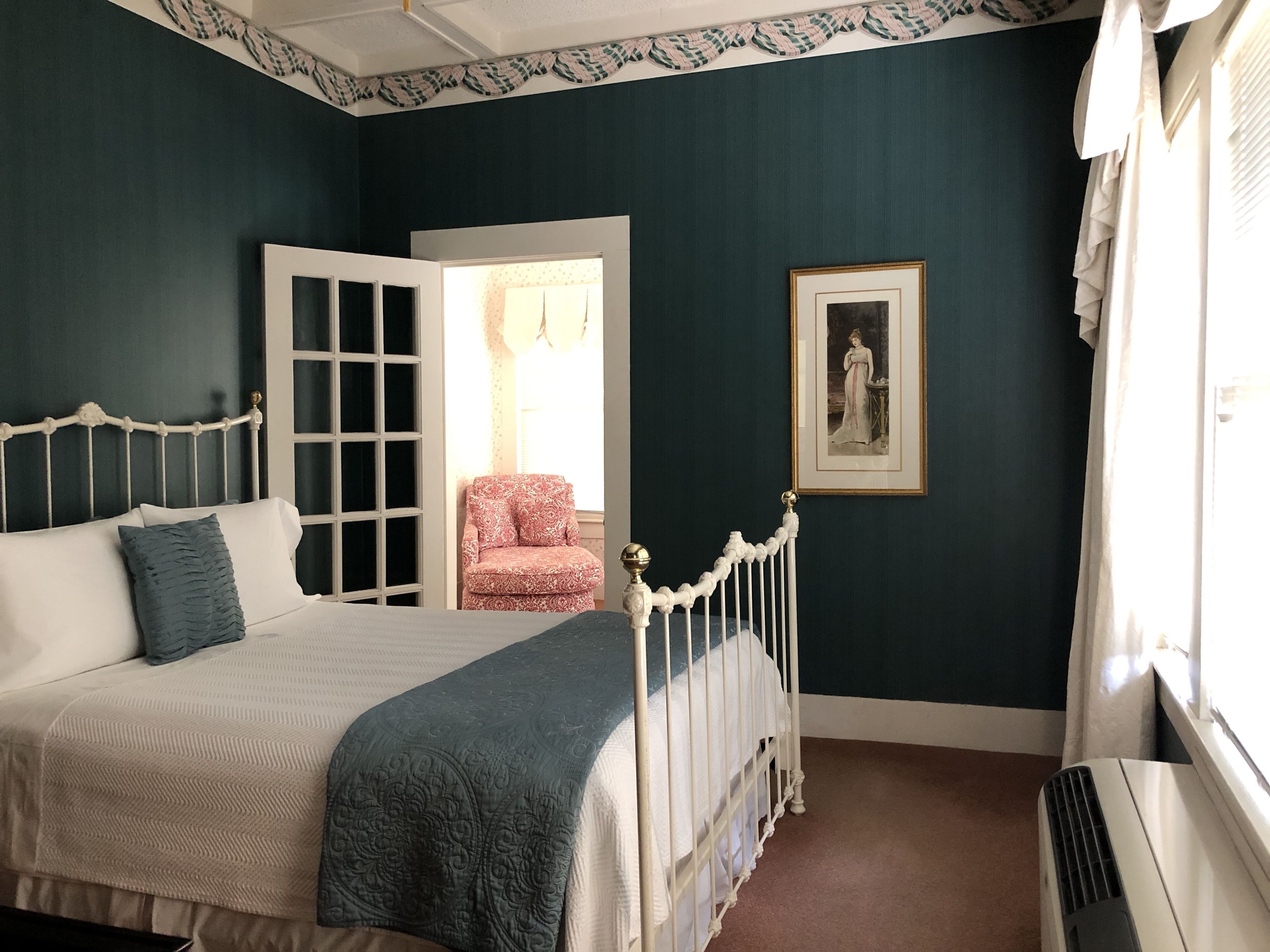 A bedroom with a bed, a chair, a radiator, and a framed picture on the wall.