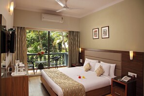 A hotel room with a bed, bedside table, and a balcony with a view of greenery. - The Hawaii Comforts (Panaji)