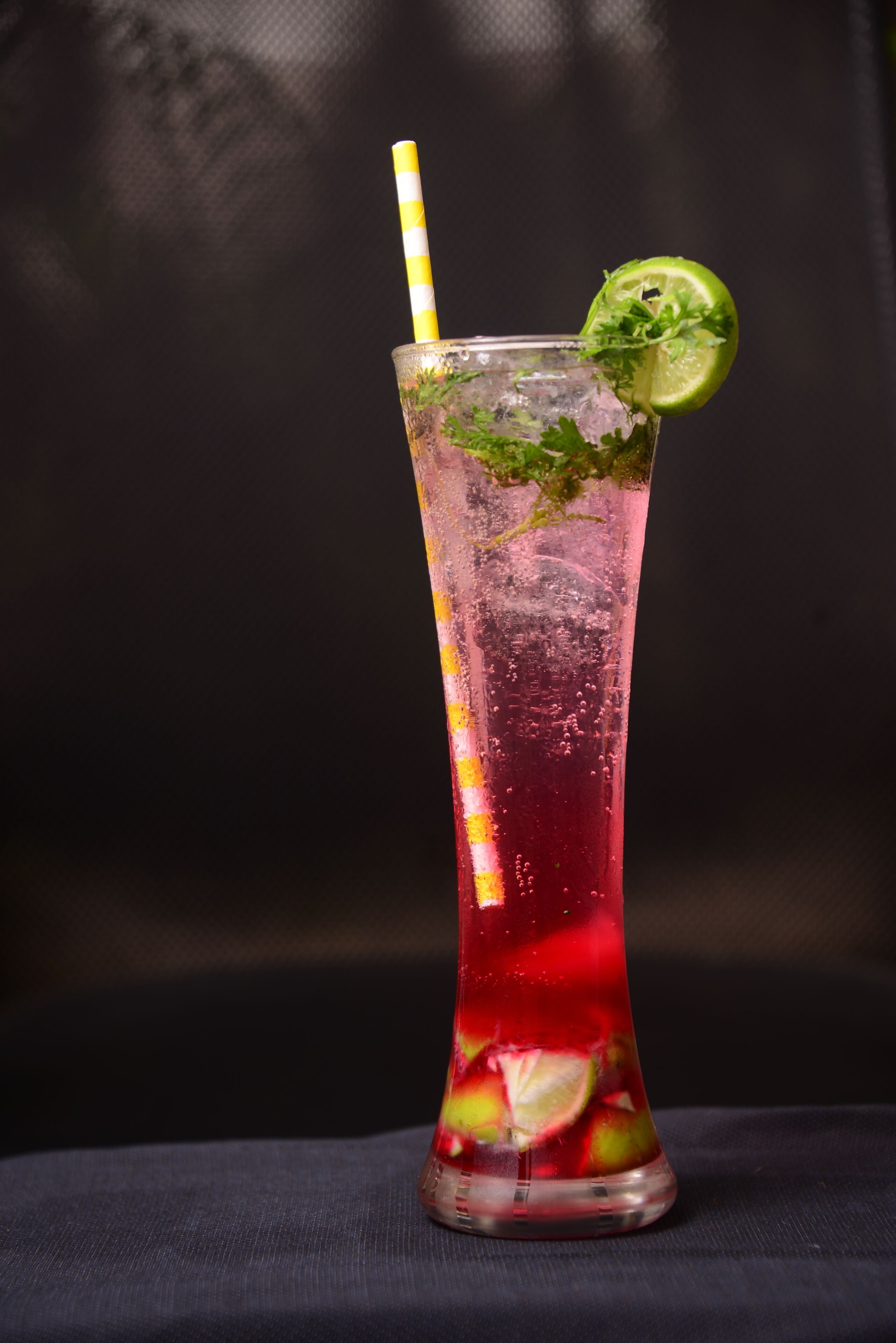 A tall glass with a lime slice and mint garnish, filled with a red beverage and ice cubes.