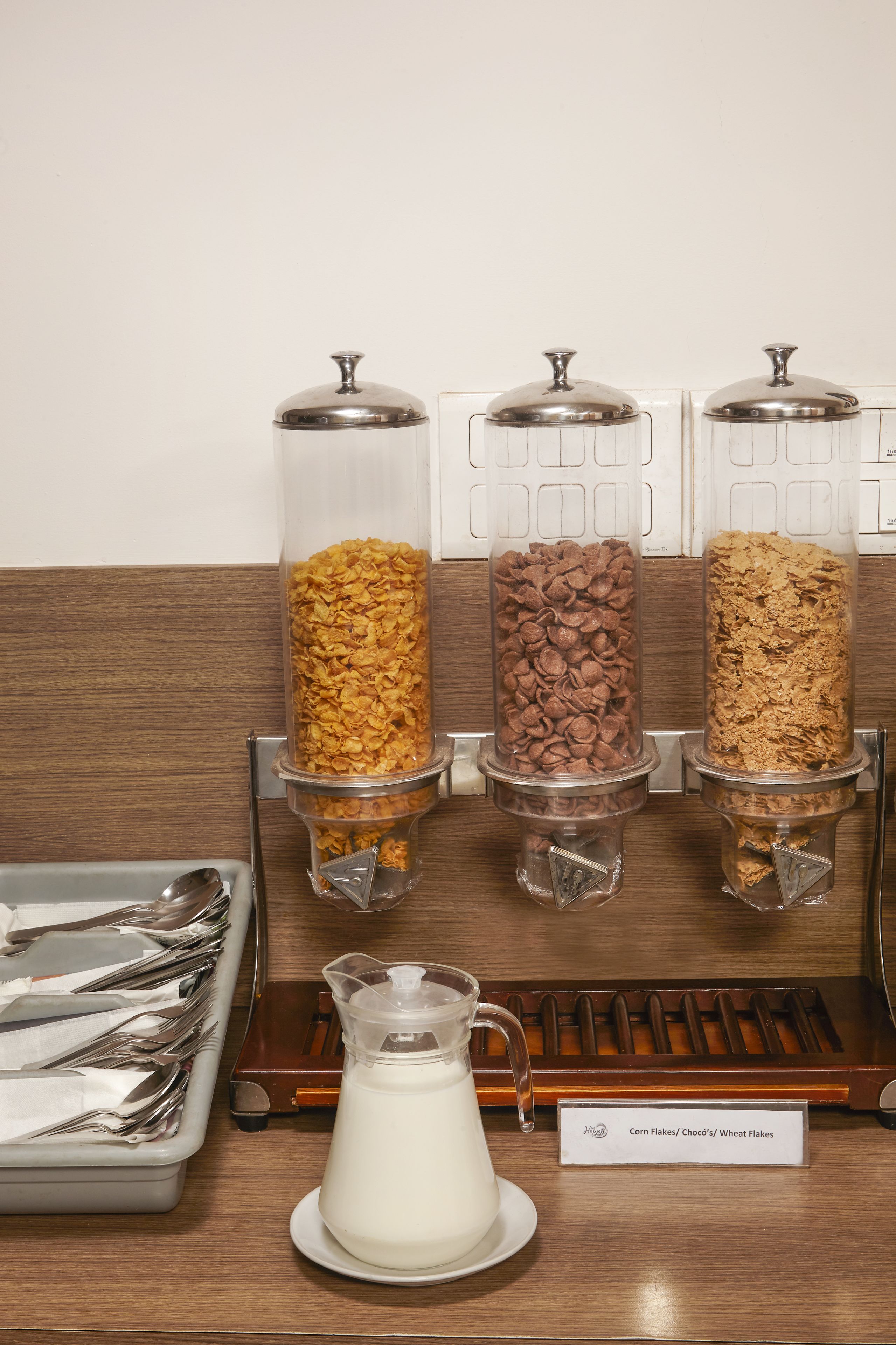 Una barra de desayuno con tres recipientes de cereal y una jarra de leche.