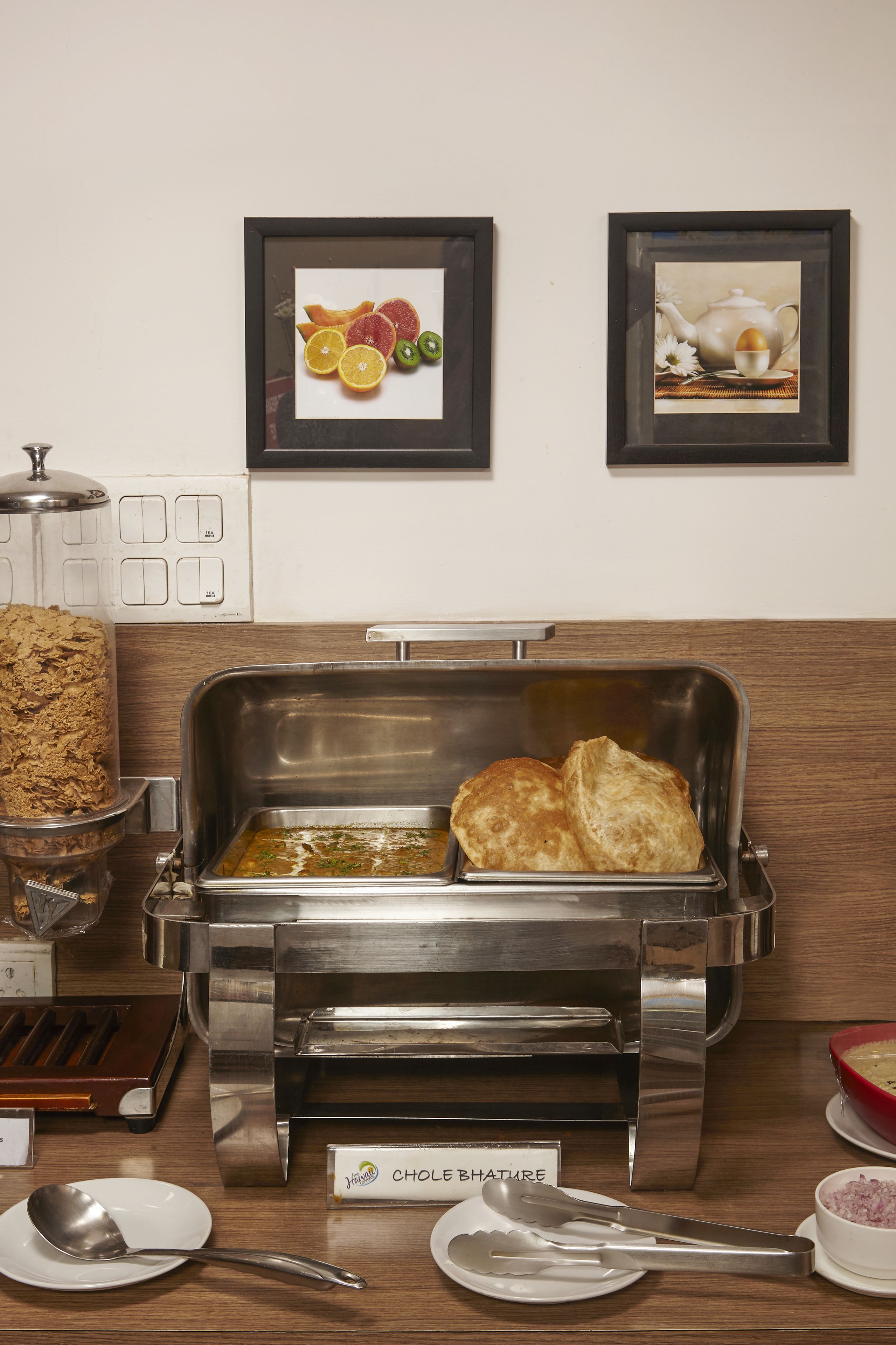A buffet setup with a meat grinder, a tray of pastries, and a sign for 'CHOLIE BHATURE'.