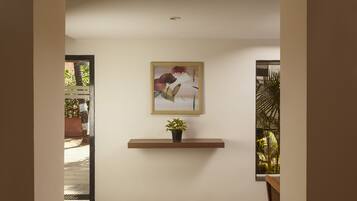 A hallway with a wooden shelf holding a potted plant and a framed picture on the wall.
