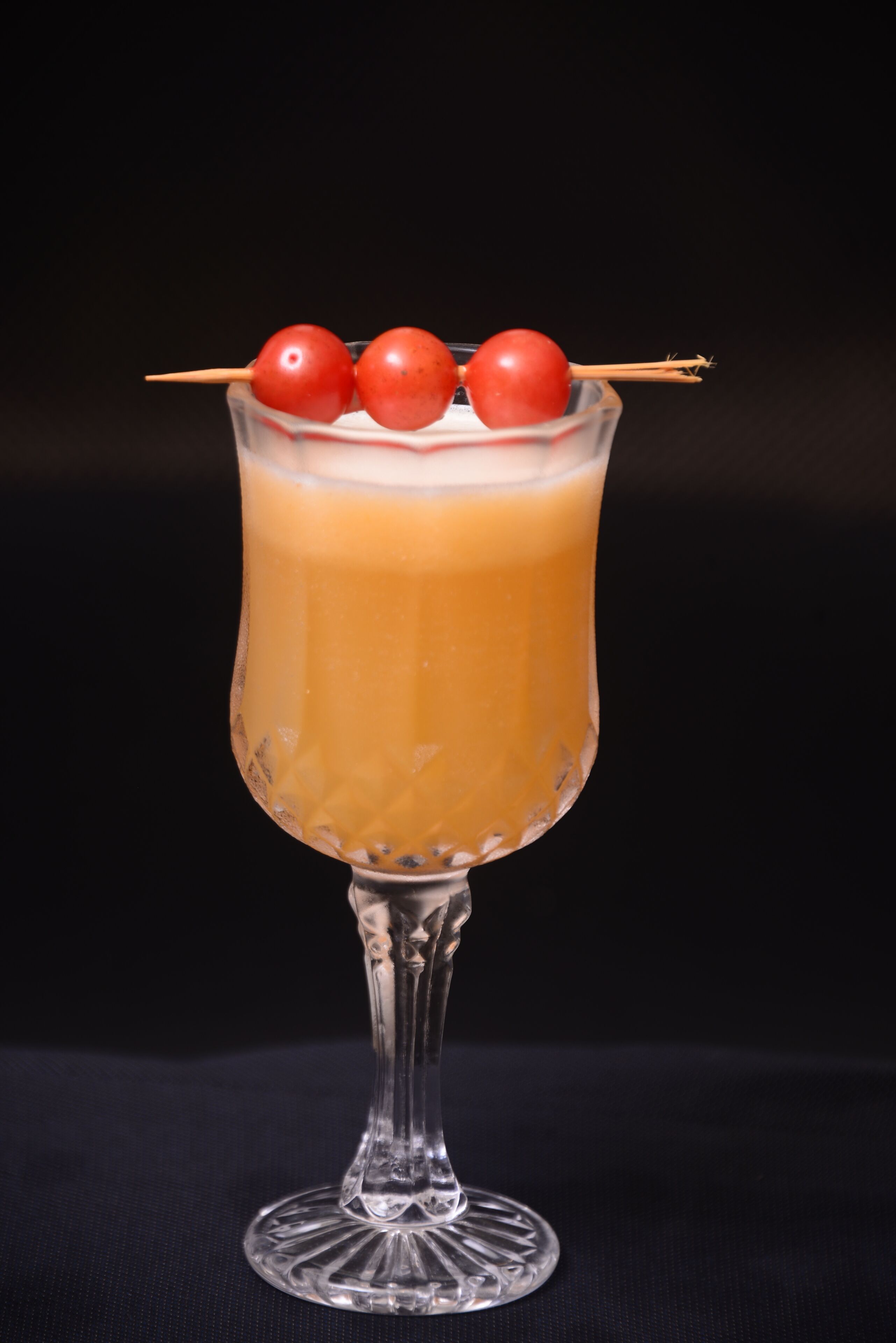 Un vaso de cóctel con tallo y pie, que contiene un líquido transparente y está adornado con tres tomatitos cherry en un palillo.