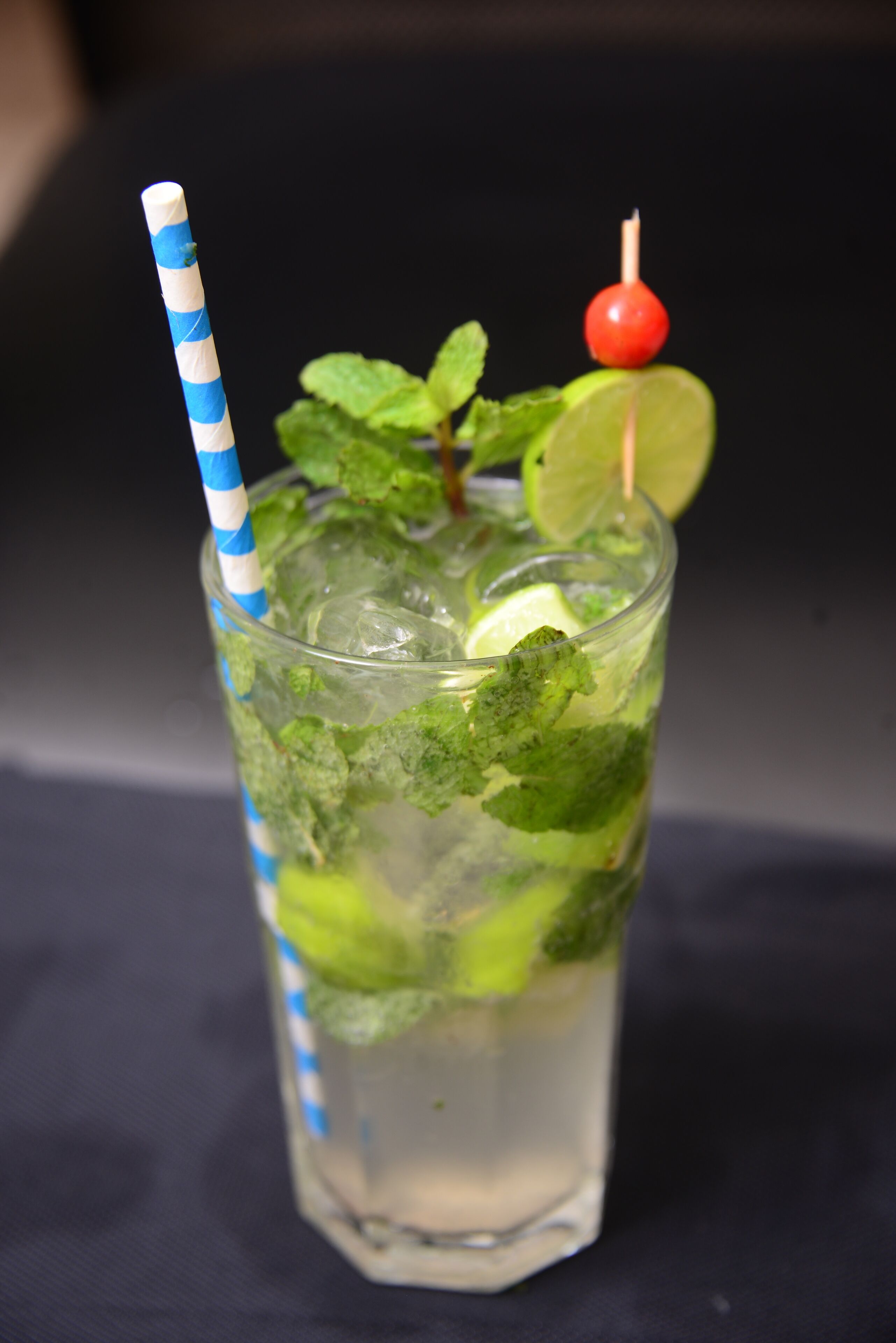 A glass of a clear beverage with mint leaves, a lime wedge, and a cherry on a skewer.