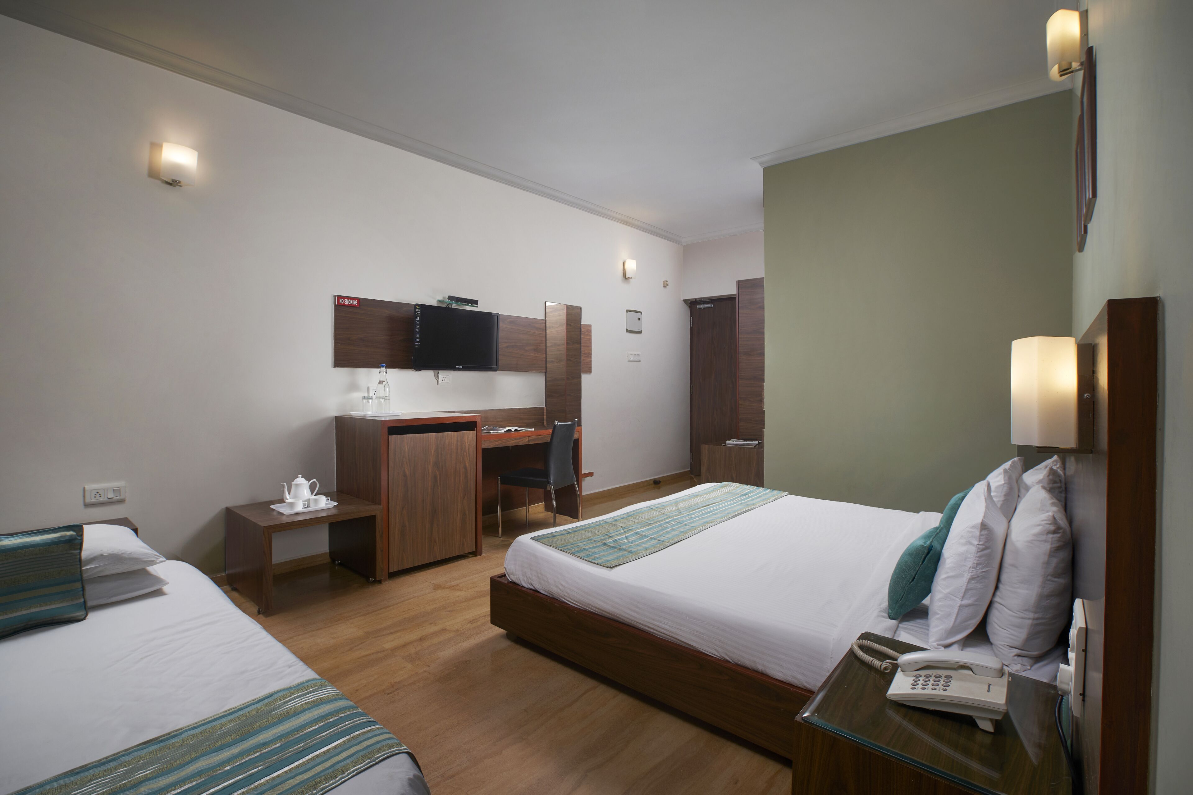 A hotel room with two beds, a desk, a chair, a telephone, and a television.