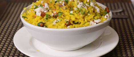 A bowl of yellow rice with herbs and nuts on a white plate.